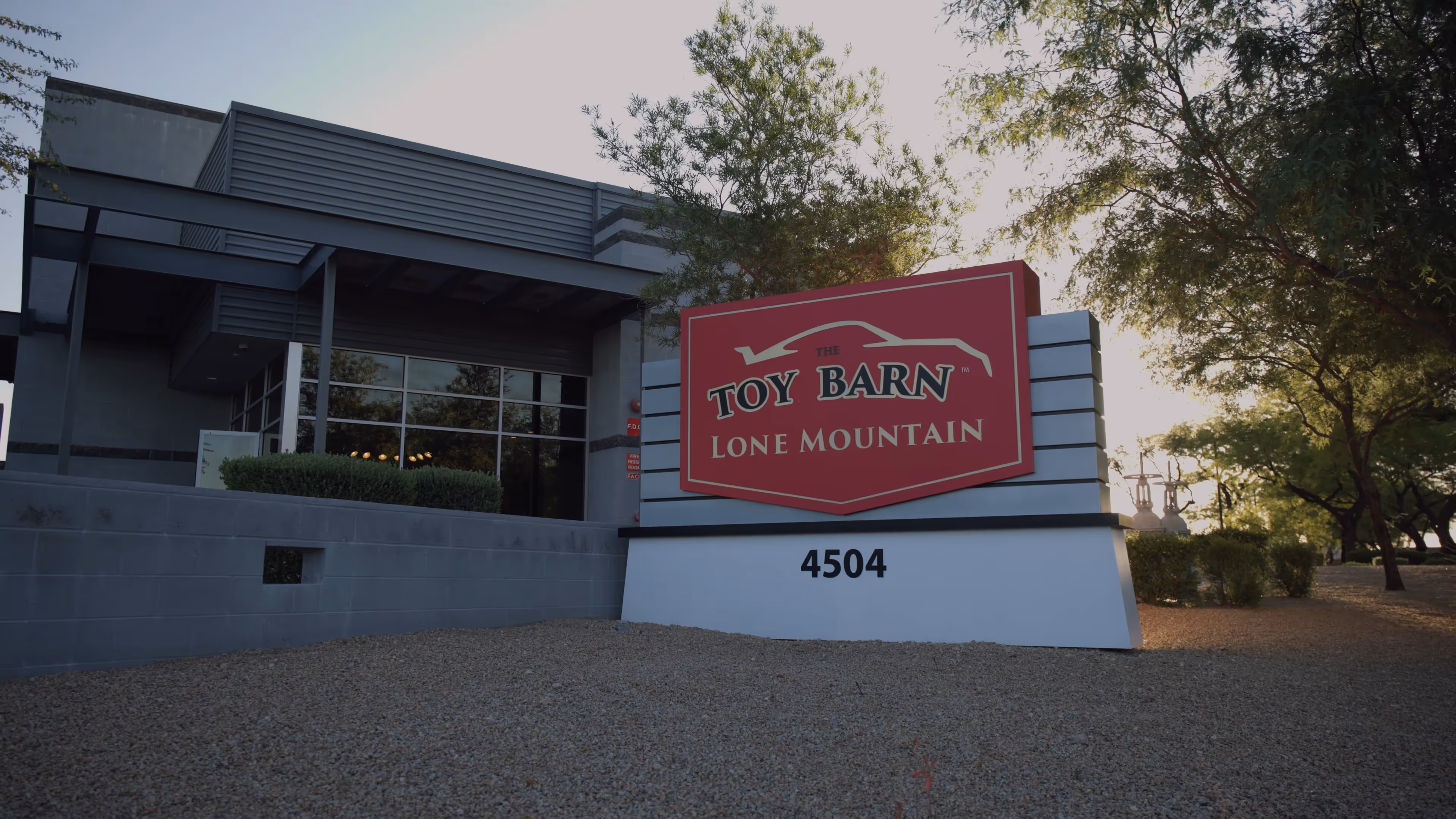 Front exterior of Toy Barn Lone Mountain dealership sign with building and trees in background.