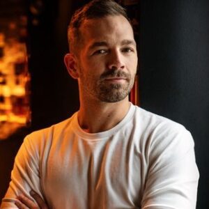 Portretfoto van man met opgerolde witte T-shirt en armen gekruist, casual zakelijke profielfoto, warme achtergrond