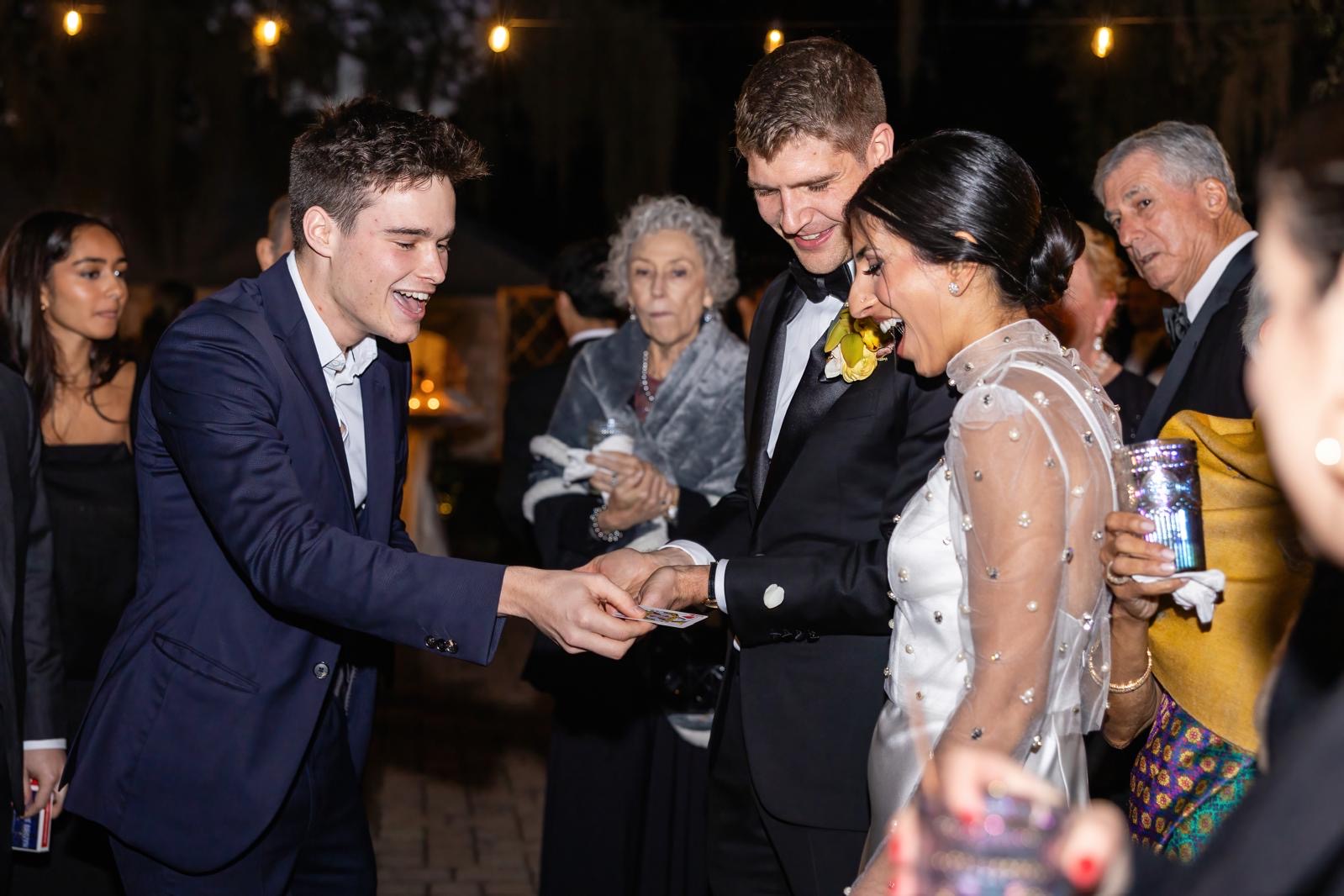 Magische act op trouwfeest, goochelaar Jonas De Bruyn voert kaarttruc uit voor bruidspaar en gasten, sfeervolle avondsetting met feestverlichting