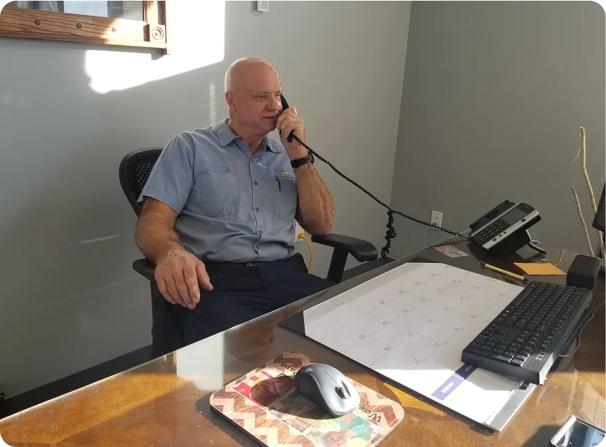 Man in a light blue button-up shirt sitting at a desk, talking on a corded office phone.