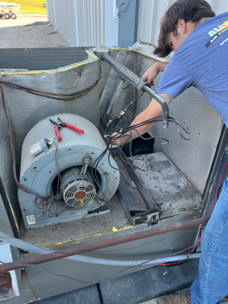Technician repairing electrical wires inside an open HVAC unit on a rooftop.