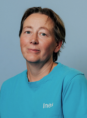 Portrait of a middle-aged person with short brown hair wearing a turquoise shirt against a blue background.