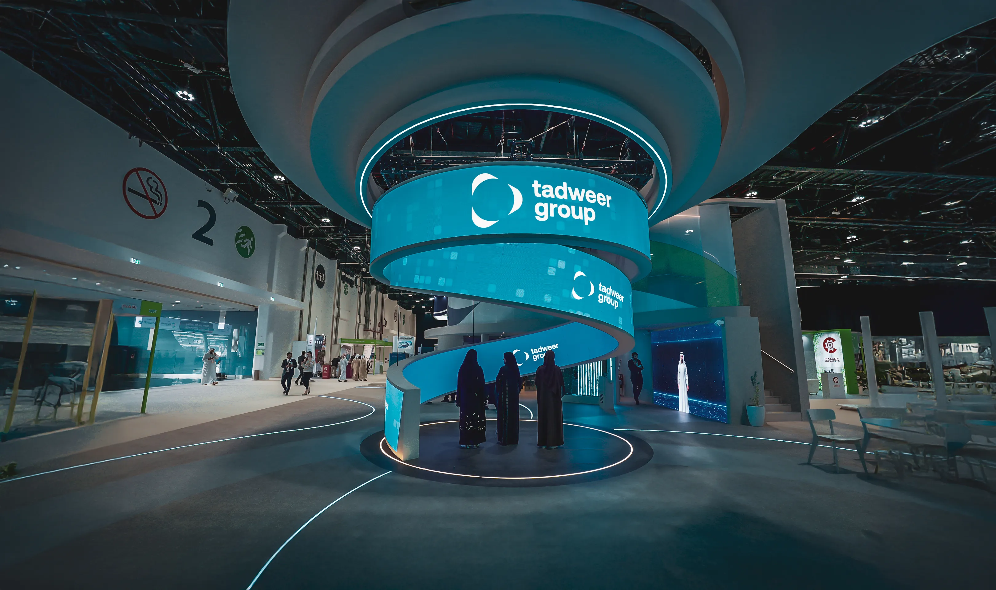 Spiral blue digital display booth with 'tadweer group' logo at an indoor exhibition hall.