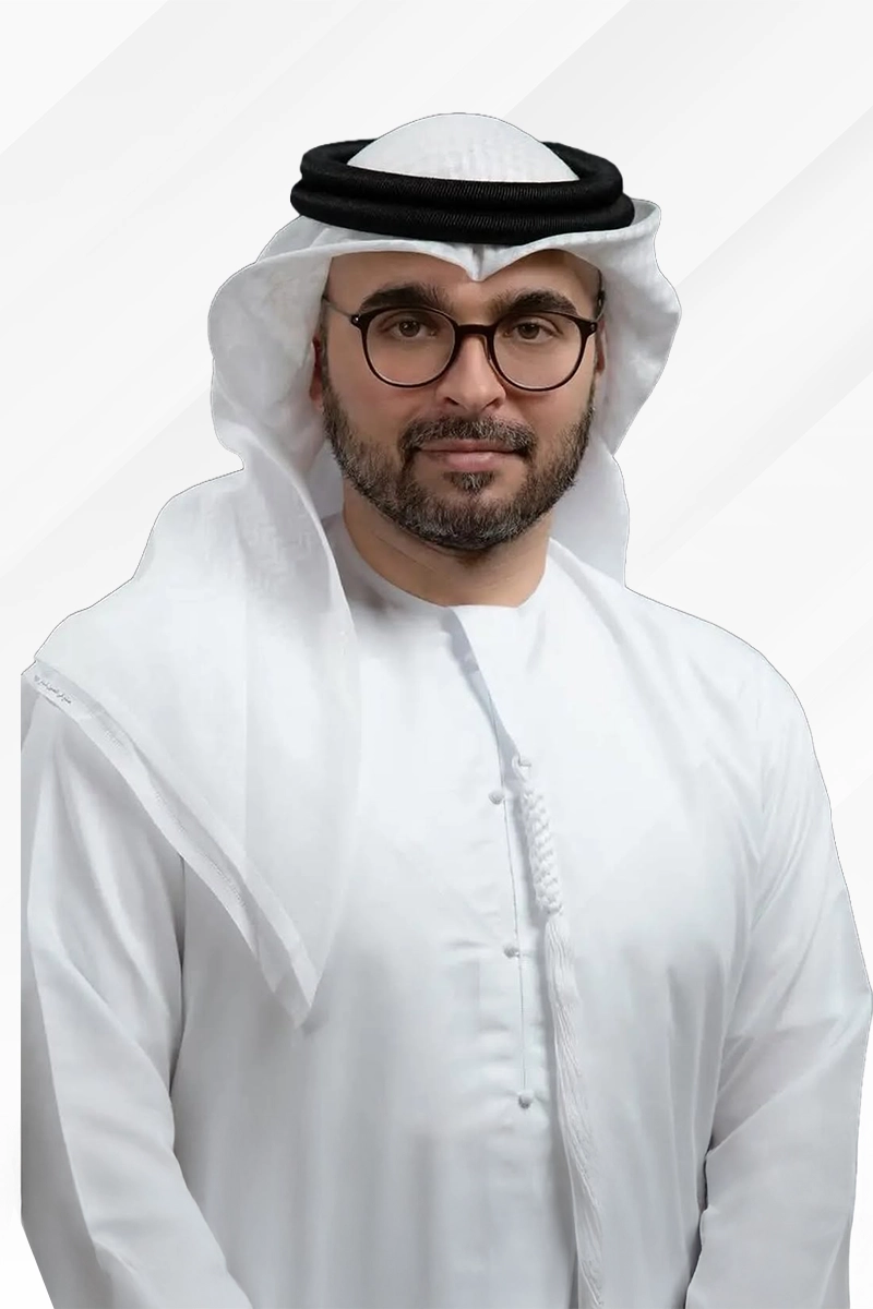 Man wearing traditional white kandura and ghutra with black agal, and glasses, smiling slightly against a light background.