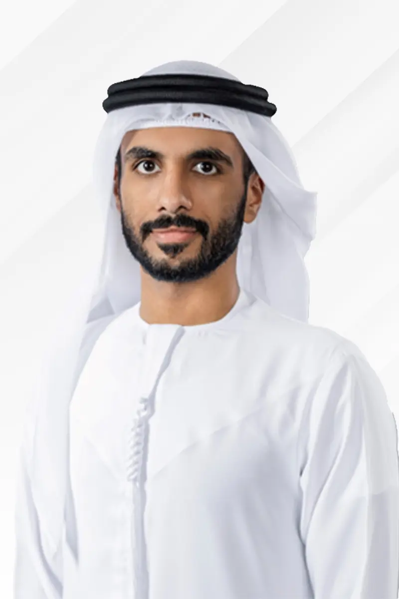 Man with a beard wearing a white kandura and a white headscarf secured with a black agal, looking at the camera.