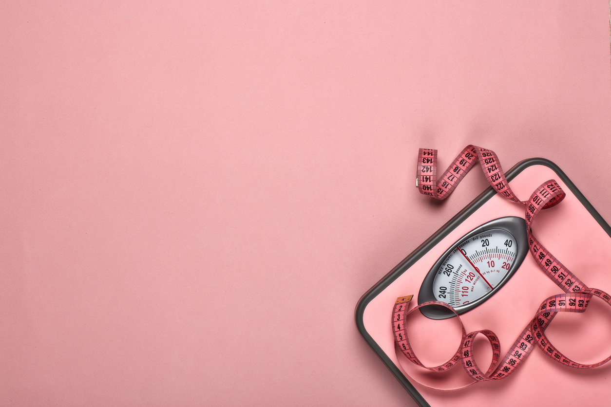 Bathroom scale with a measuring tape placed on a pink background.