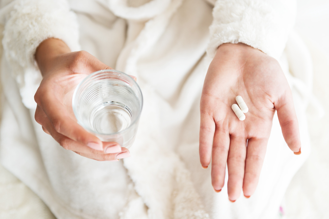 Low-dose naltrexone capsules held in hand beside a glass of water, representing supervised dosing and treatment through HealthHub.