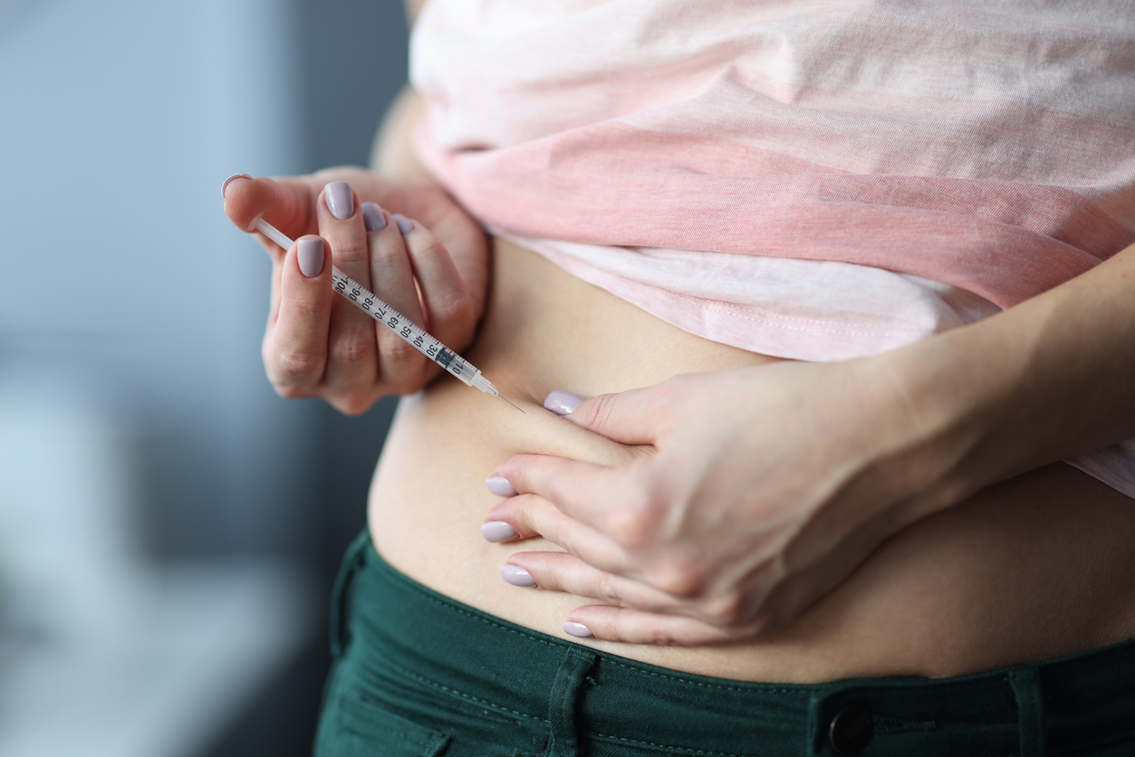 Person administering an abdominal injection at home as part of a prescribed injectable medication routine.