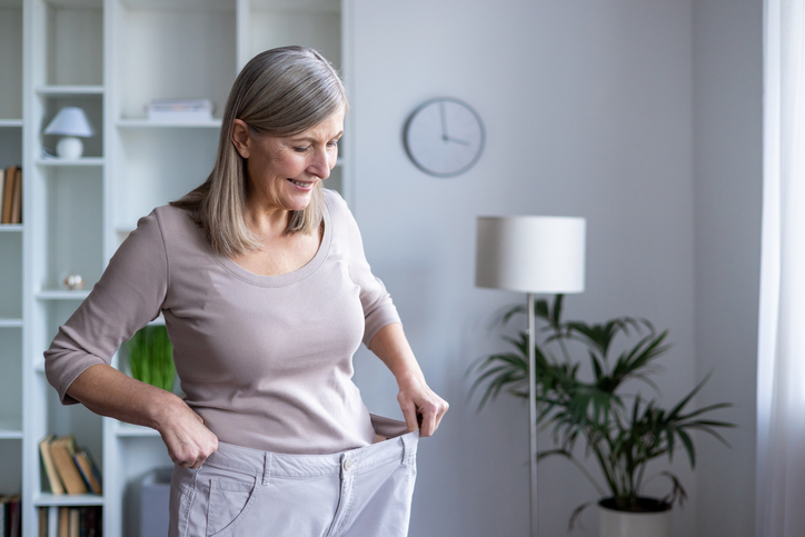 Woman holding the waistband of oversized jeans, representing weight-loss progress achieved through GLP-1 medication and healthy lifestyle changes.