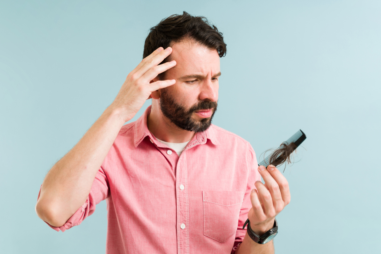 A man looking concerned while holding a comb filled with shed hair, illustrating early signs of hair loss in the 30s.
