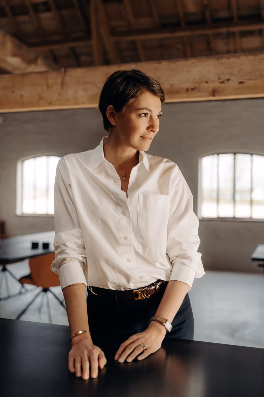 Professionele vrouw in een wit hemd in een stijlvol kantoor met houten details en daglicht.