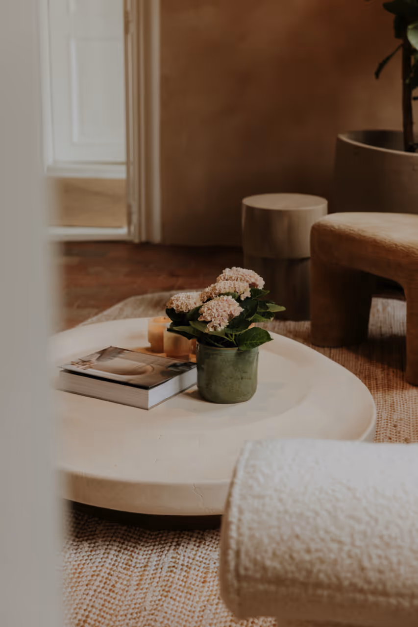 Stijlvolle woonkamer met ronde salontafel, vaas met bloemen, kaarsen en designstoelen in een warm interieur.