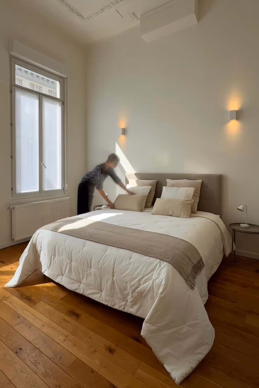 Stijlvolle lichte slaapkamer met houten vloer en opgemaakt bed met neutrale tinten en decoratieve kussens.