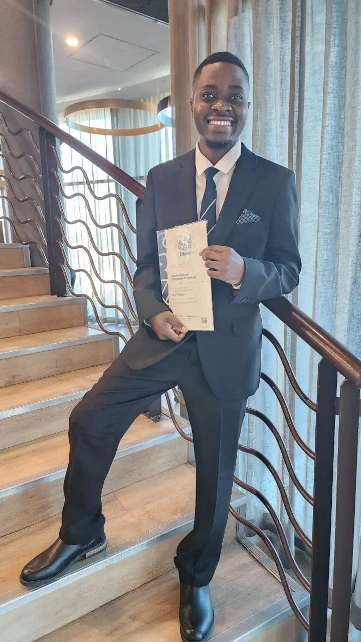 Smiling man in a dark suit standing on stairs holding a certificate.