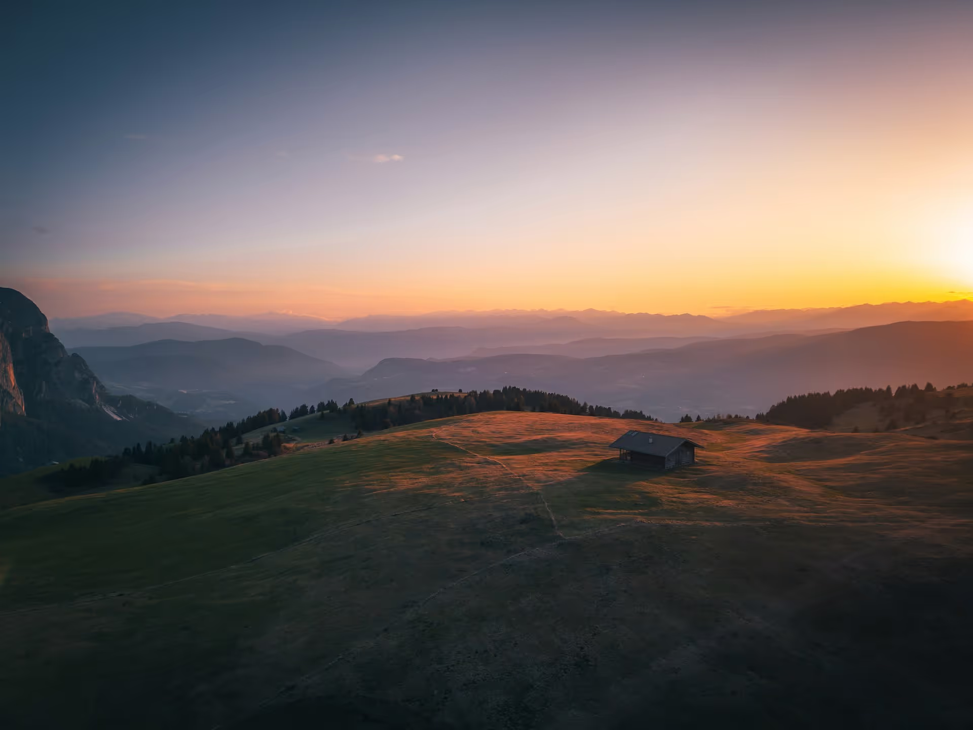 Sunset over rolling hills with a solitary cabin casting long shadows.