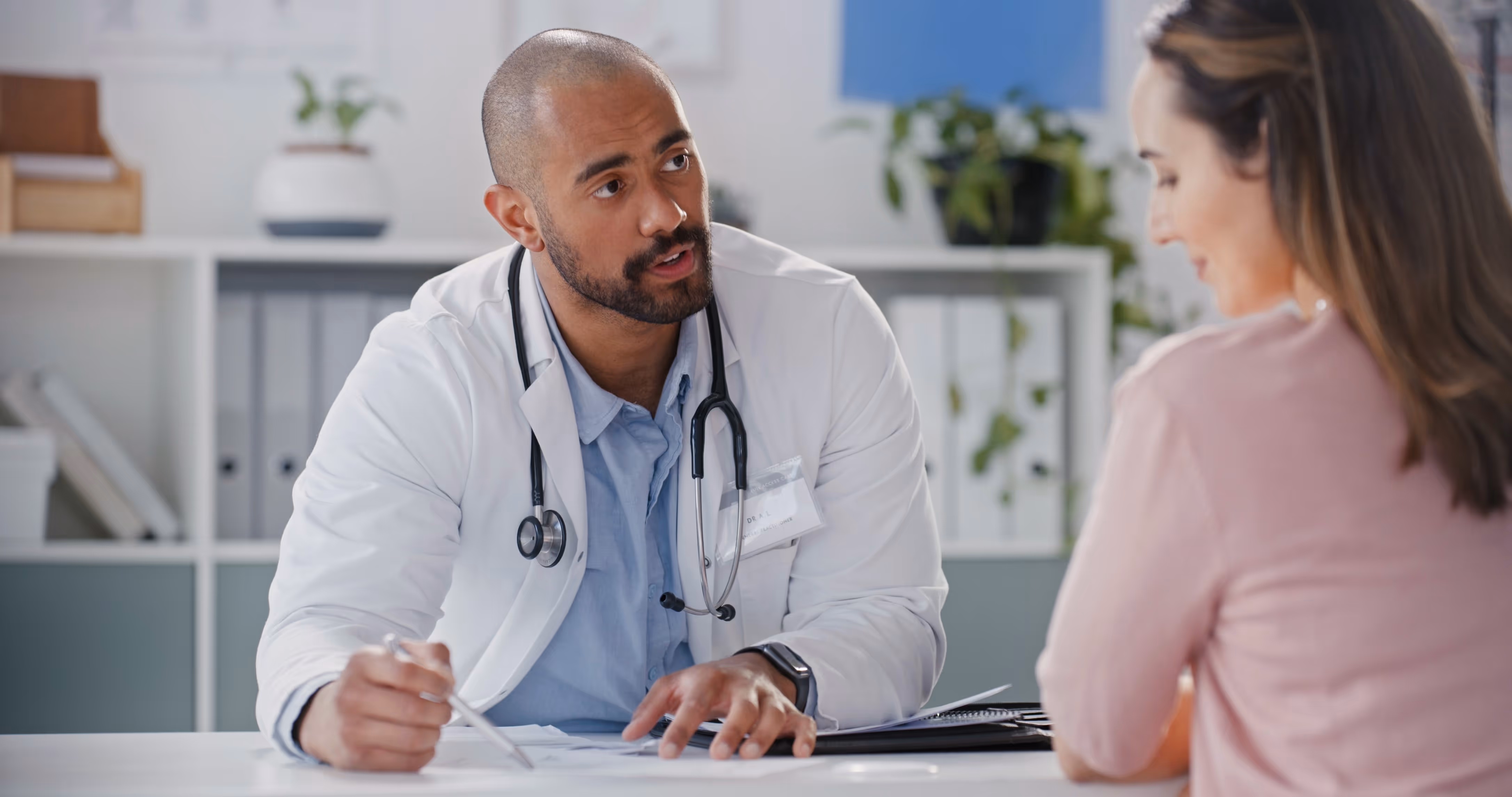 Male doctor in white coat consulting with a female patient in a medical office.