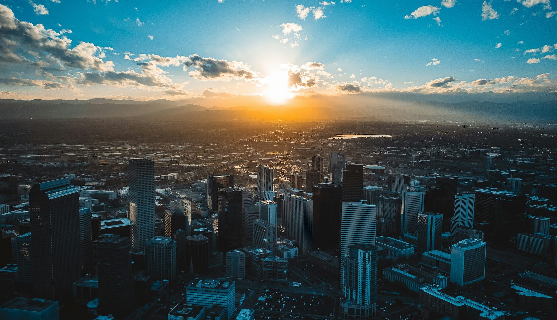 Aerial view of downtown Denver at sunset with the Rocky Mountains beyond.