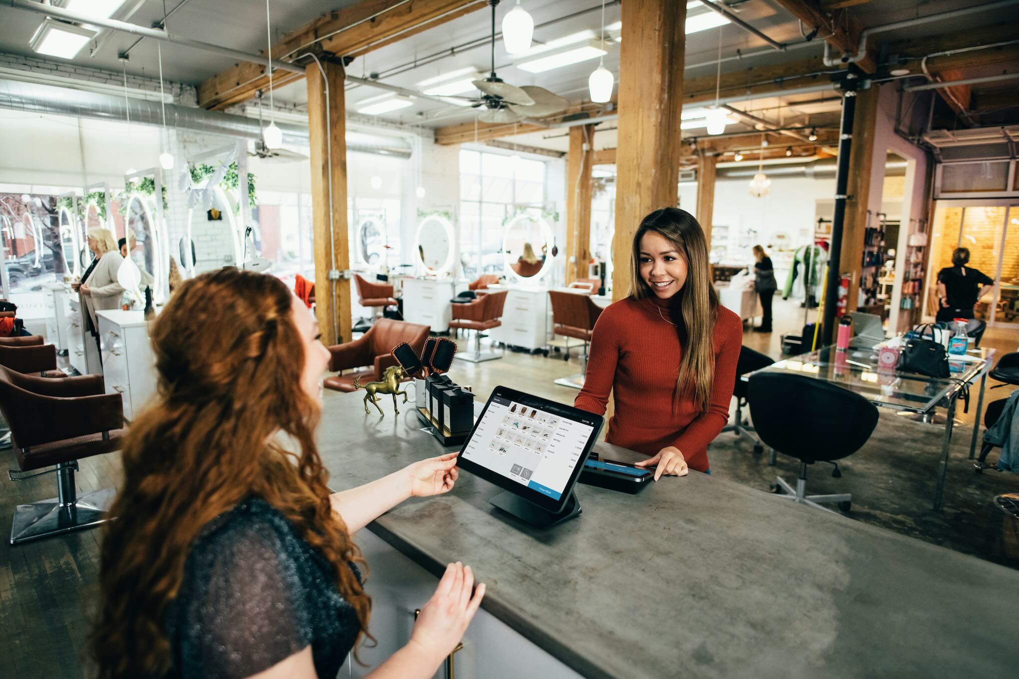 Customer checking out at a modern salon front desk with a tablet point-of-sale.