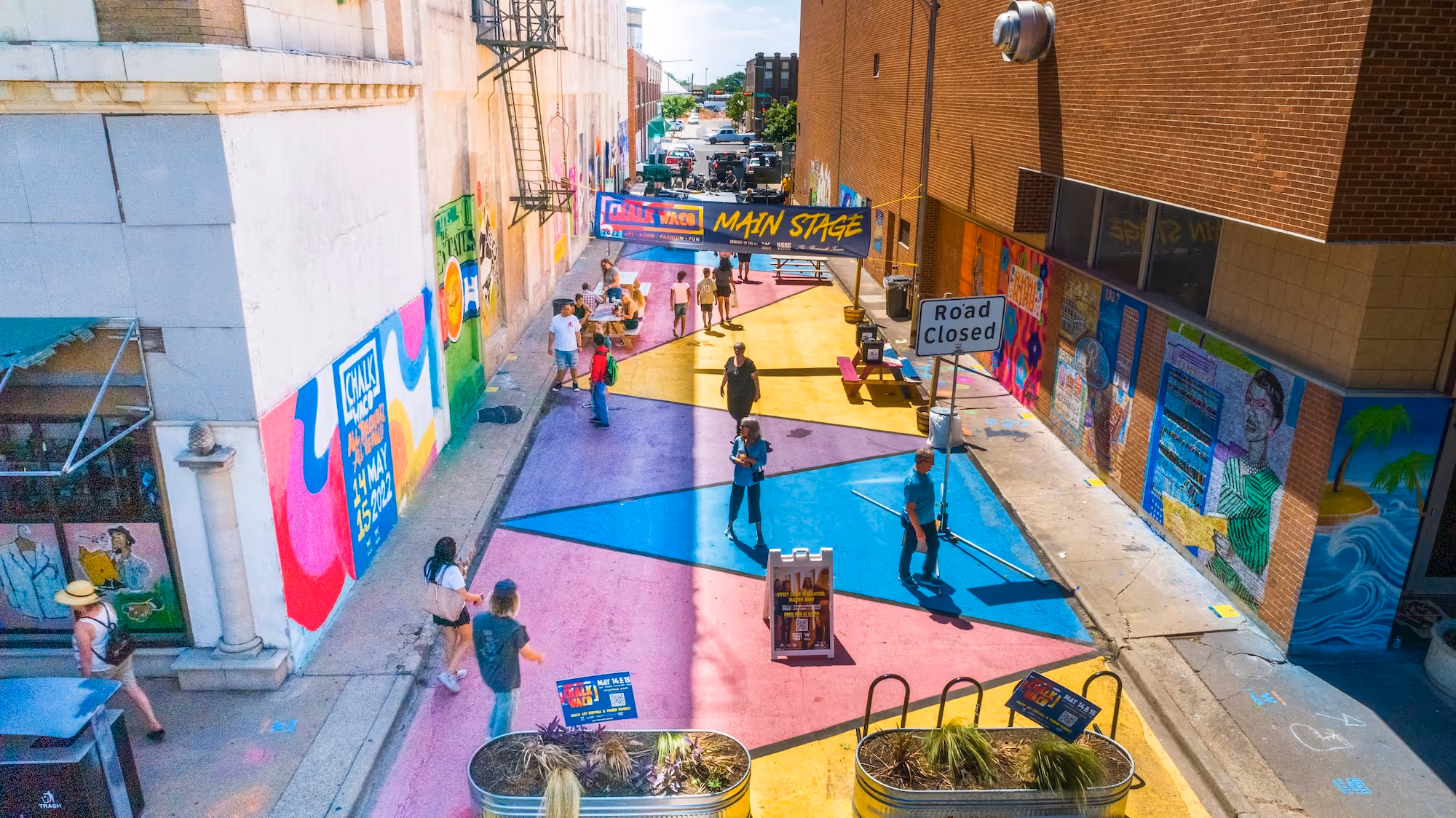 Colorful urban street closed off for a public event with people walking and murals on the walls.