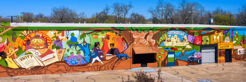 Colorful mural on a long wall depicting themes of unity, education, community, history, and celebration including books, graduates, historical buildings, and a grocer store.
