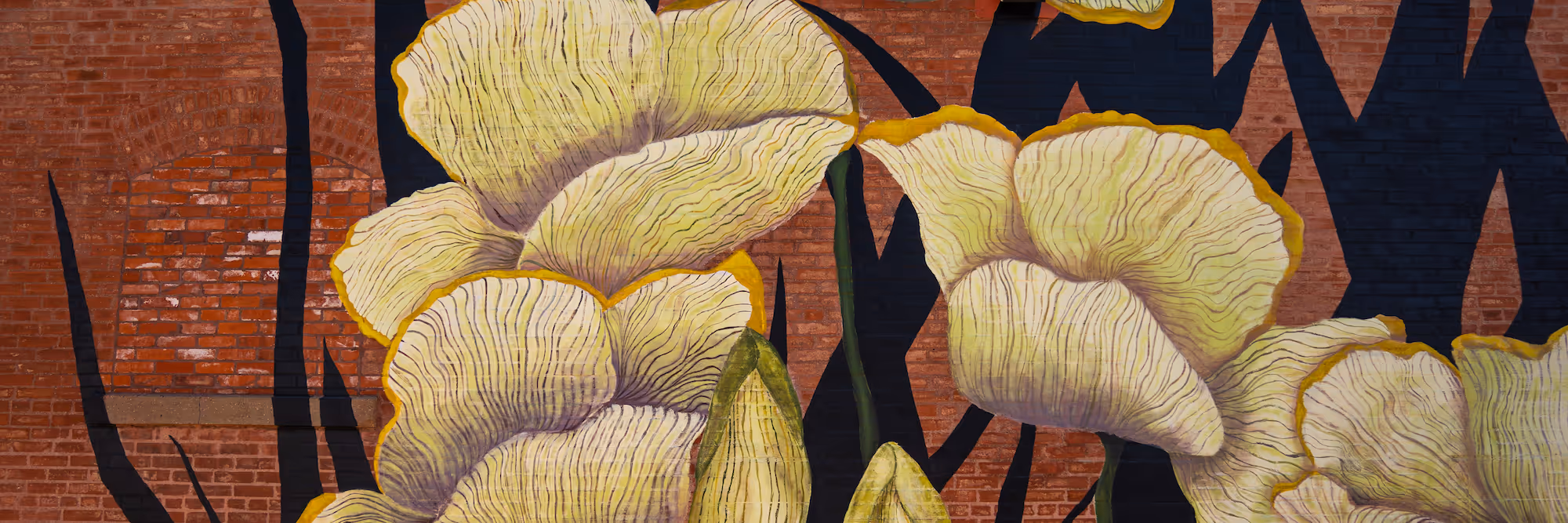 Mural of large yellow flowers with black stems painted on a red brick wall.