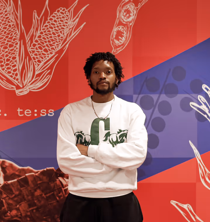 Man with folded arms standing in front of a red and blue wall with white botanical illustrations and text.