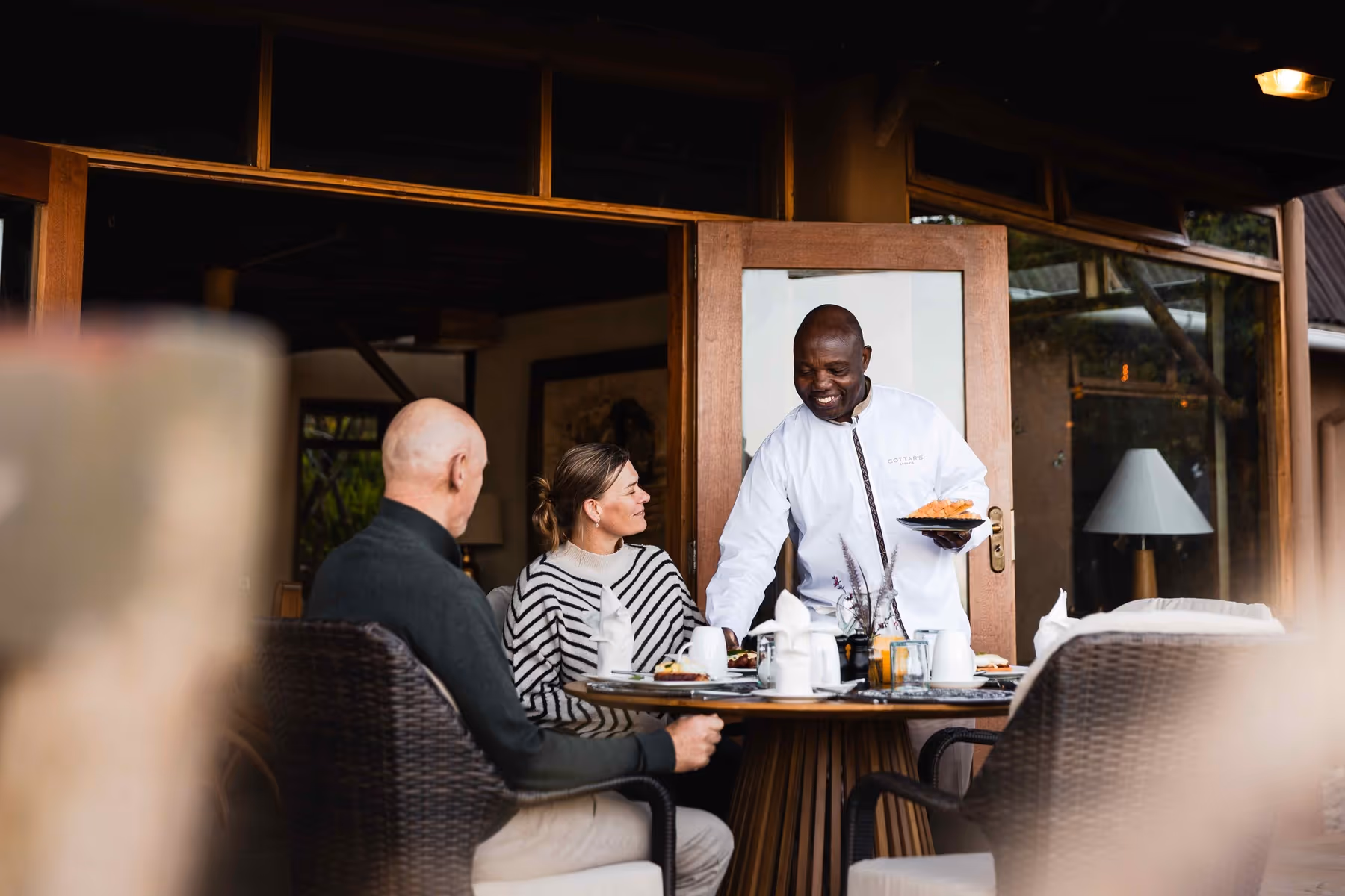 A butler warmly serves breakfast to guests on a veranda — a glimpse into the personalized hospitality that defines Cottar’s. The setting is intimate yet sophisticated, showcasing the human touch behind each guest experience.