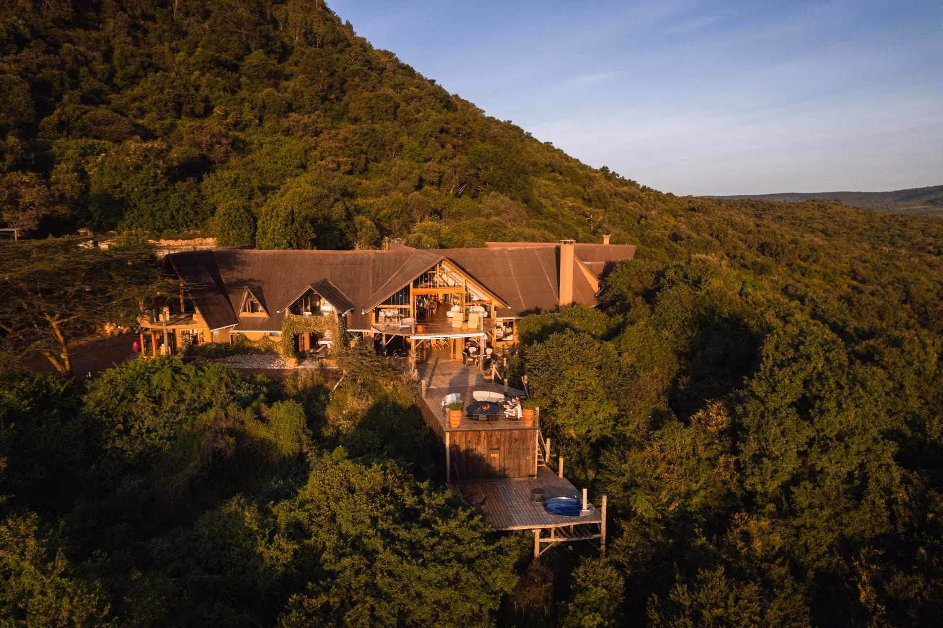 Aerial view of Cottar’s Bush Villa surrounded by lush forested hills in the Olderkesi Conservancy, Maasai Mara.