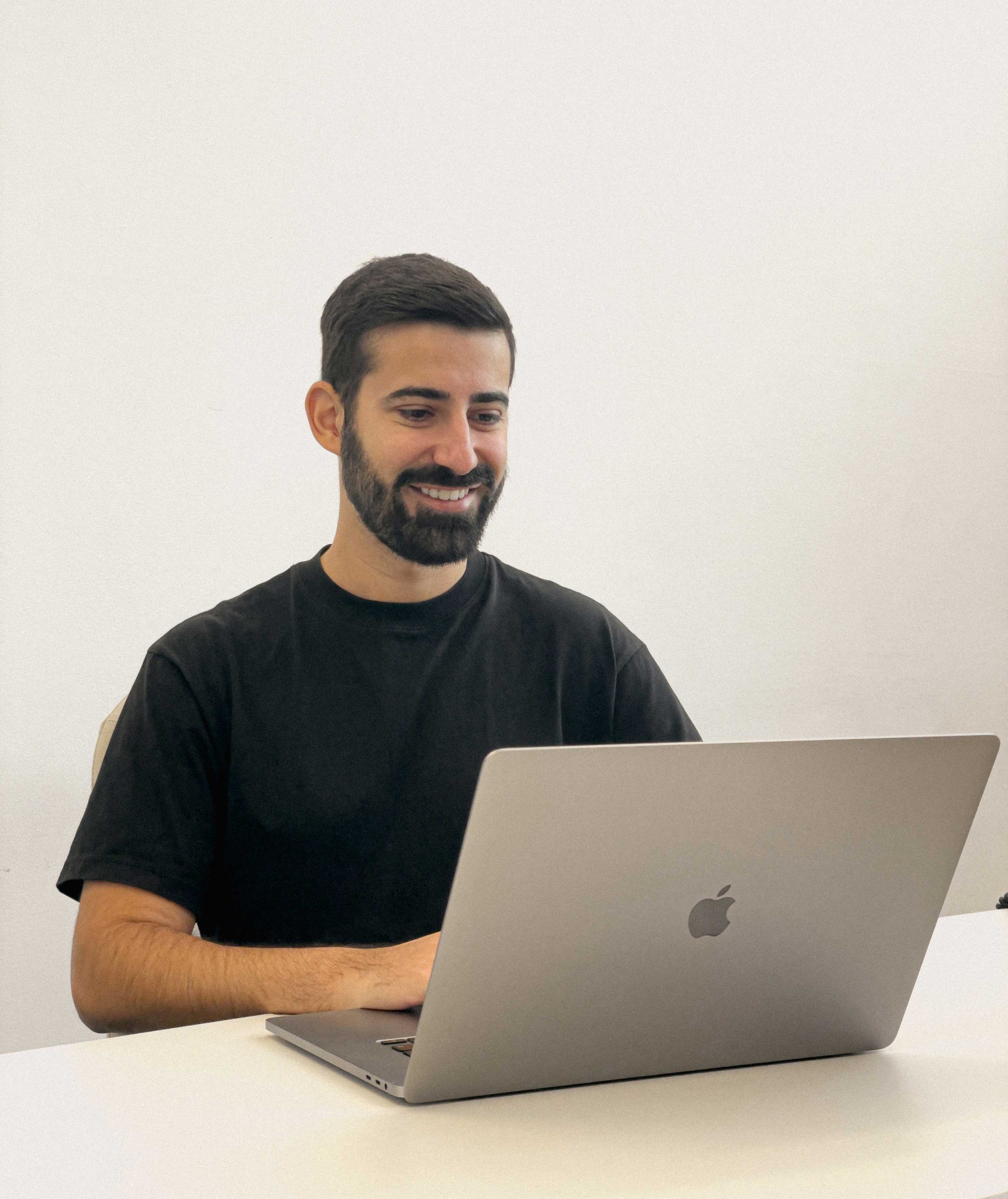 Valerio Colazingari, Kola Design Studio founder, working on a sleek silver MacBook at a minimalist white desk in a modern office