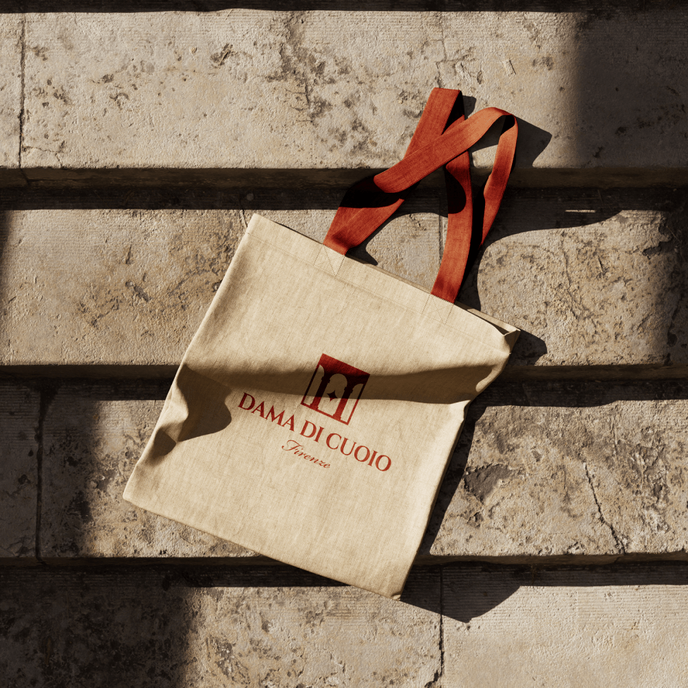 Dama di Cuoio branded canvas tote bag with Florence leather goods logo design and orange ribbon handles on stone background