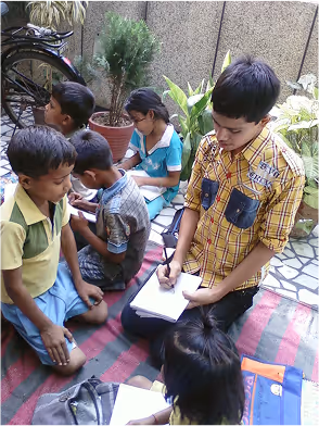 Children studying together outdoors on colorful mat surrounded by plants