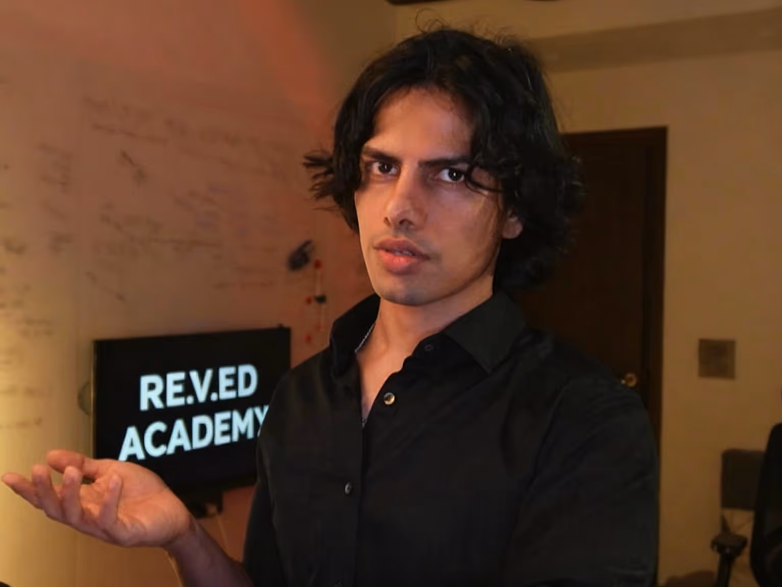 Gesturing person in black shirt standing near Rev.ed Academy sign