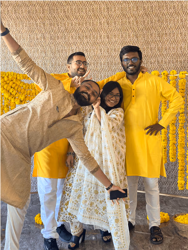 Four friends in yellow and white traditional attire pose playfully together