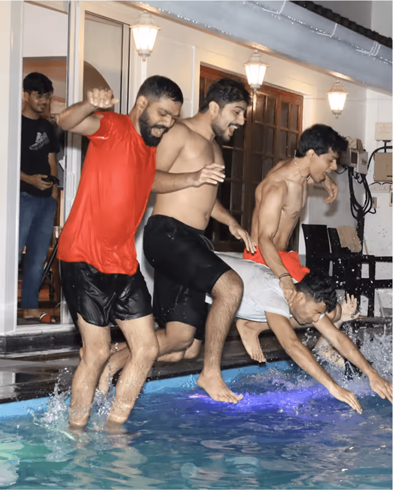 Group of men playfully pushing each other into an indoor swimming pool