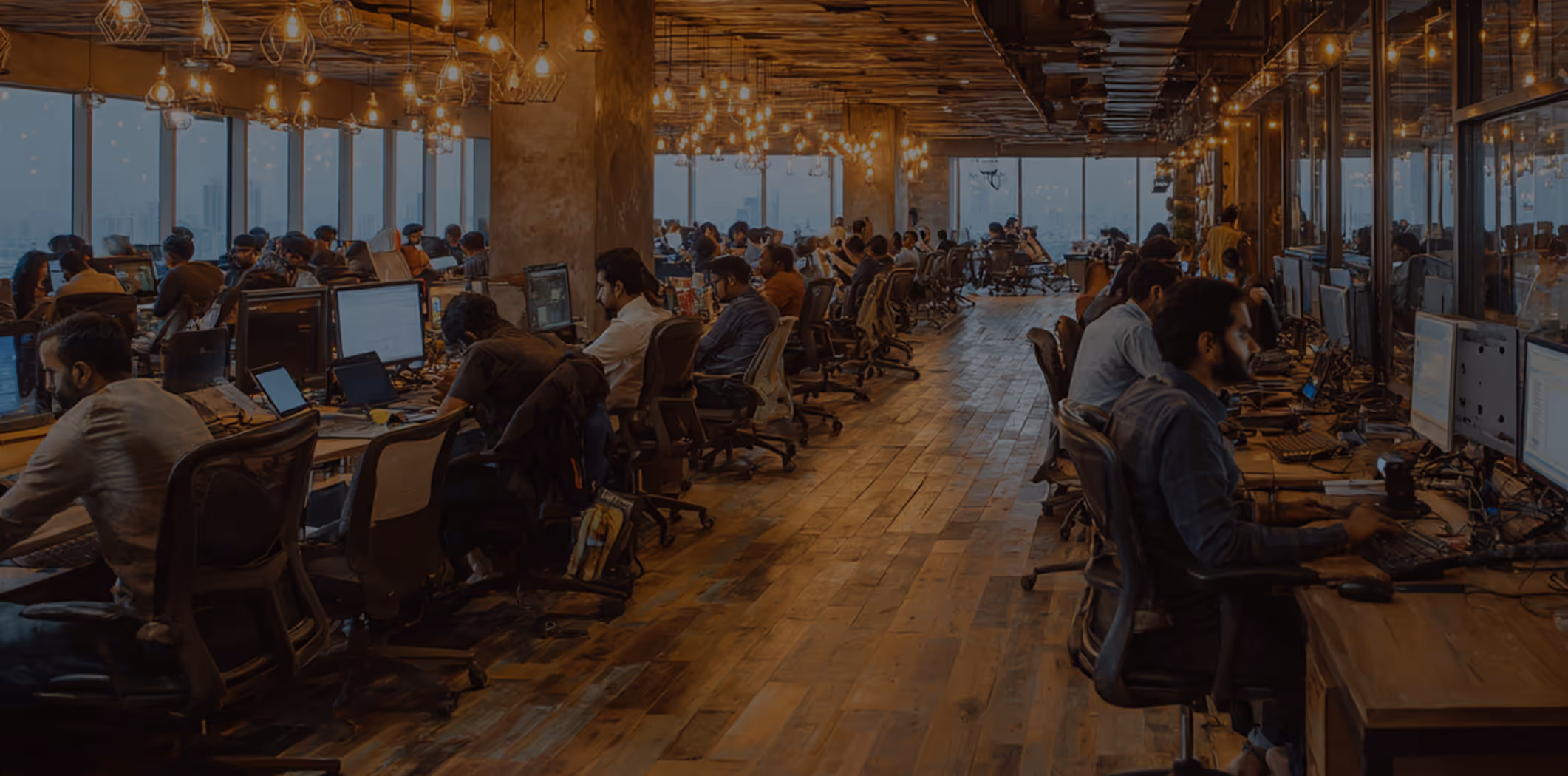 Modern open office workspace with workers at computers and hanging lights