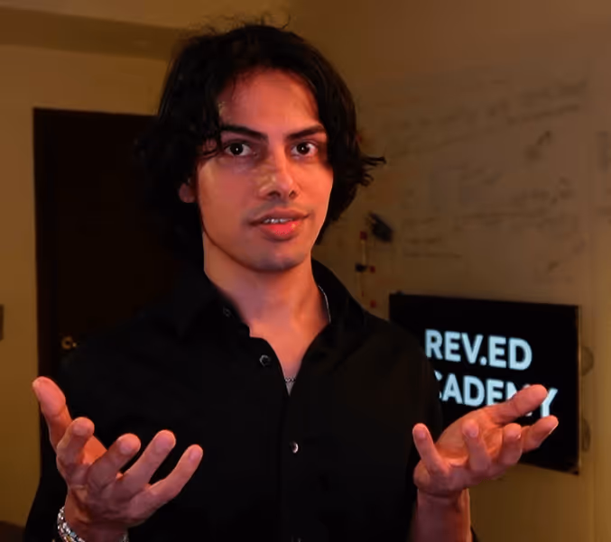 Person in black shirt gesturing while standing in front of blurred sign