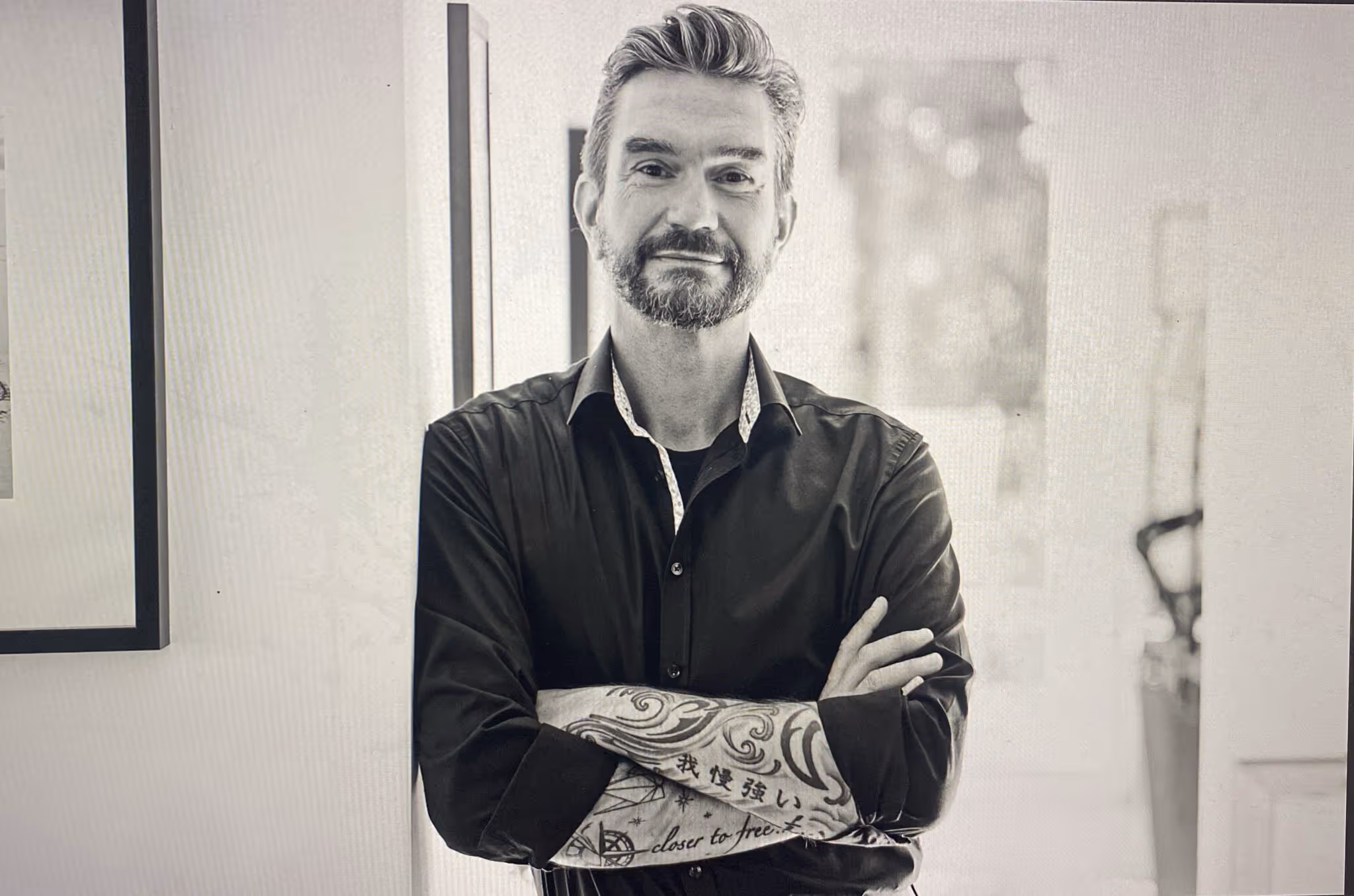 Der Leadership Rebell - Ein Mann mit Bart und kurzen Haaren trägt ein schwarzes Hemd und zeigt tätowierte Unterarme mit Schriftzeichen und Mustern.
