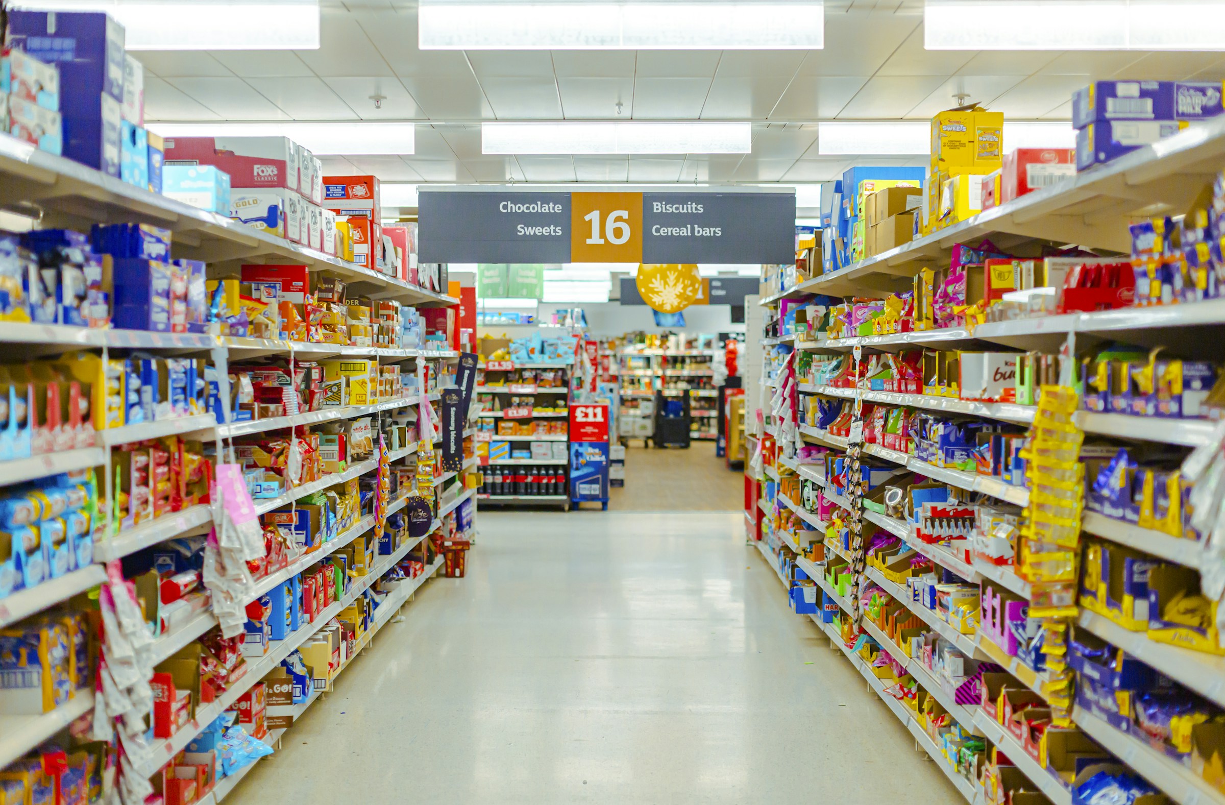 Packaged foods lining both sides of a brightly lit supermarket aisle
