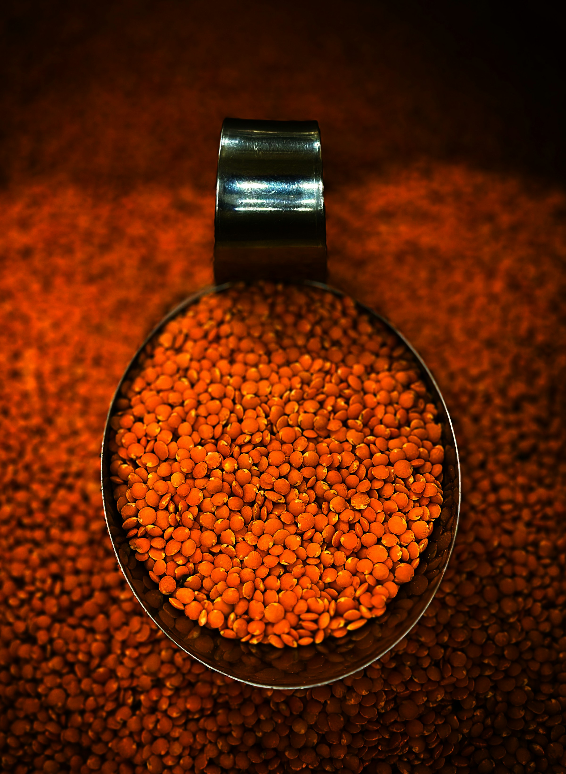 A metal scoop filled with red lentils on a textured market surface