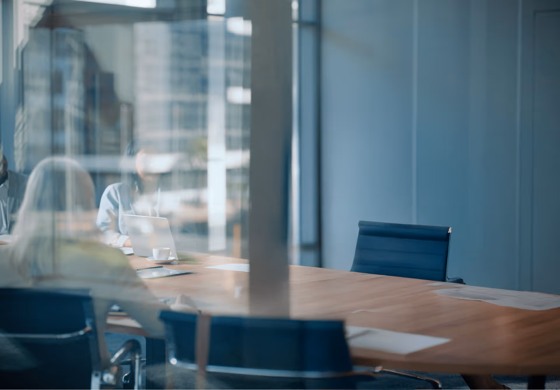 Reflection of people in a meeting room with blue chairs and a wooden conference table.