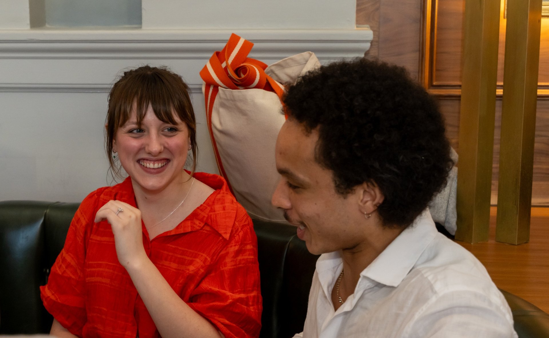 Smiling woman in red shirt and man in white shirt engaged in conversation on a couch.