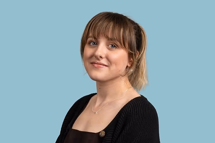 Young woman with bangs and a ponytail wearing a black sweater and necklace against a blue background.