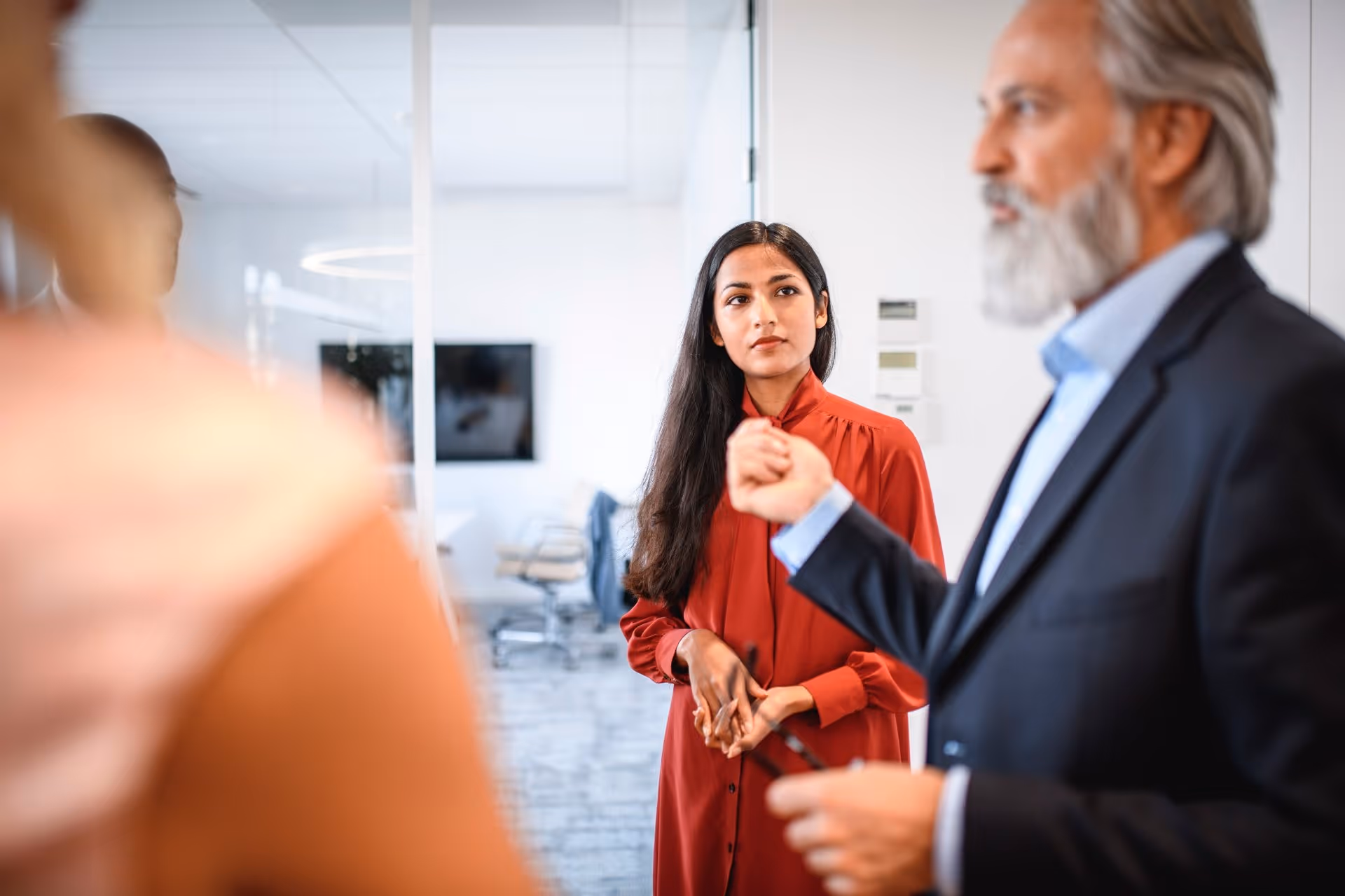 Woman in red dress attentively listens to a man speaking in a professional office setting.