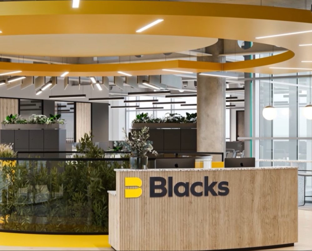 Modern office reception desk with Blacks logo and plants behind glass partition.
