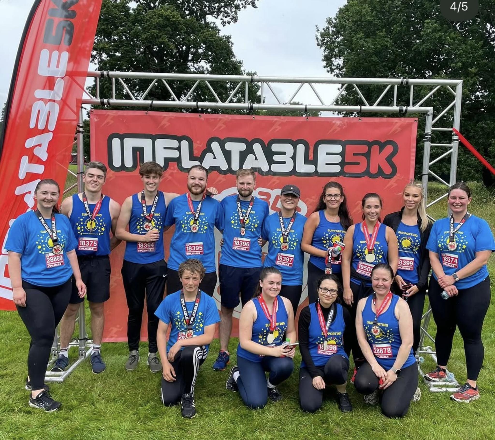 Group of runners wearing blue shirts posing with medals after completing the Inflatable 5K race.