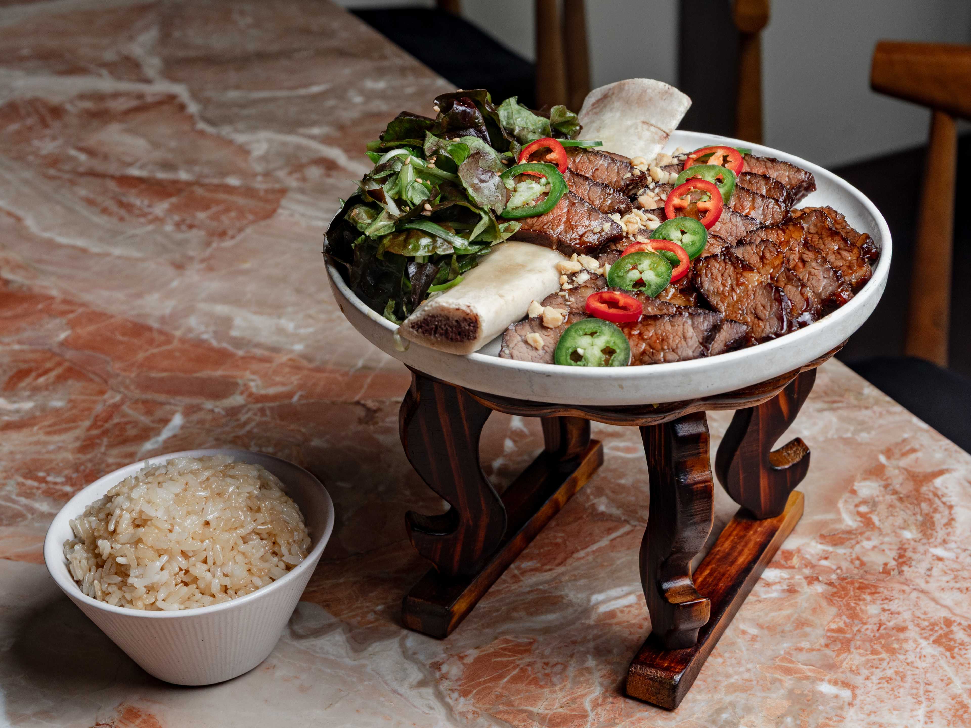 Hojokban New York Hojok Galbi, sliced bone-in Korean short rib on a wooden pedestal with scallion salad