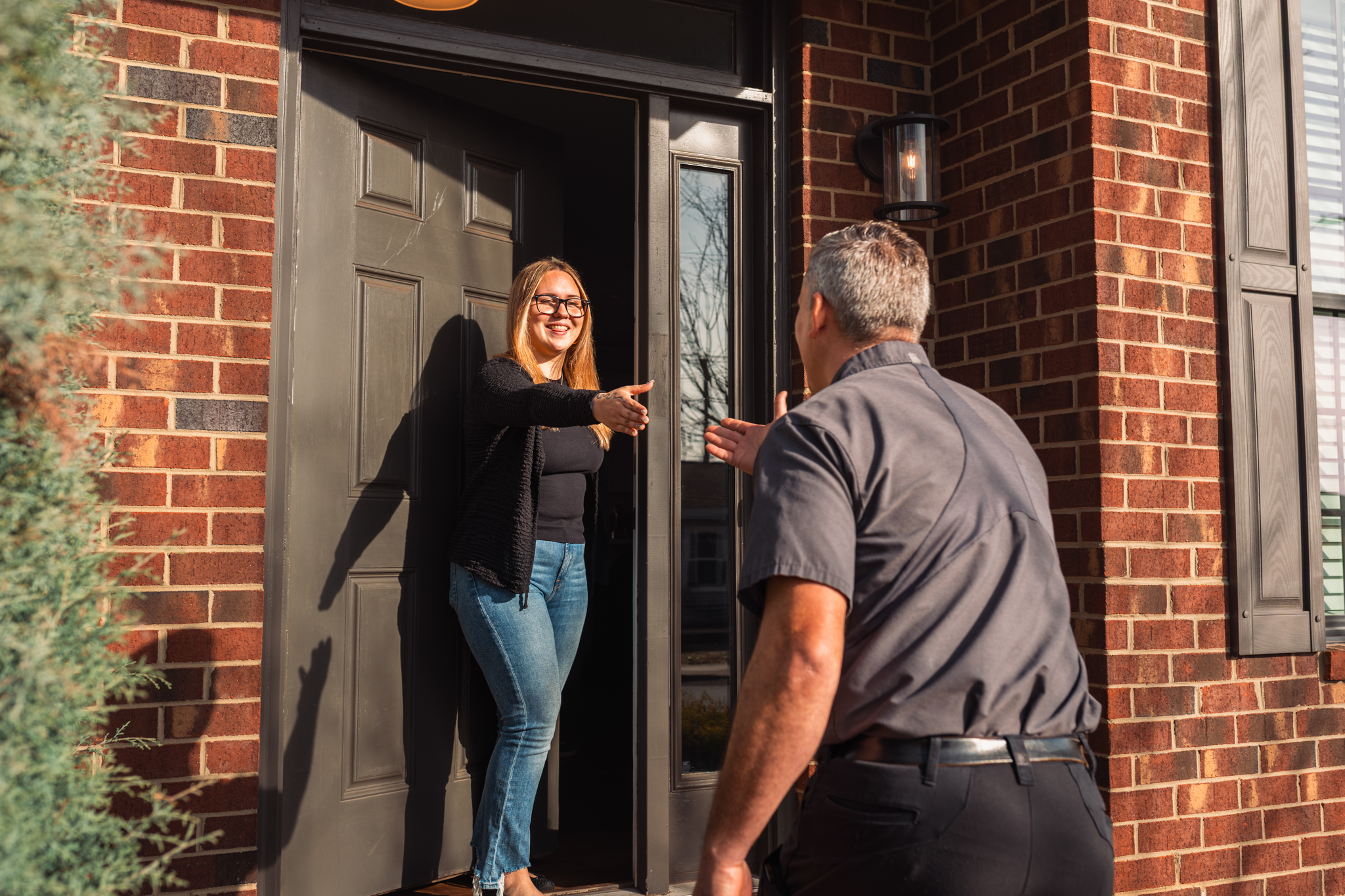 Charlotte Mechanical technician Raynor meeting a customer at the front door of their home, reaching forward to shake hands with the customer.