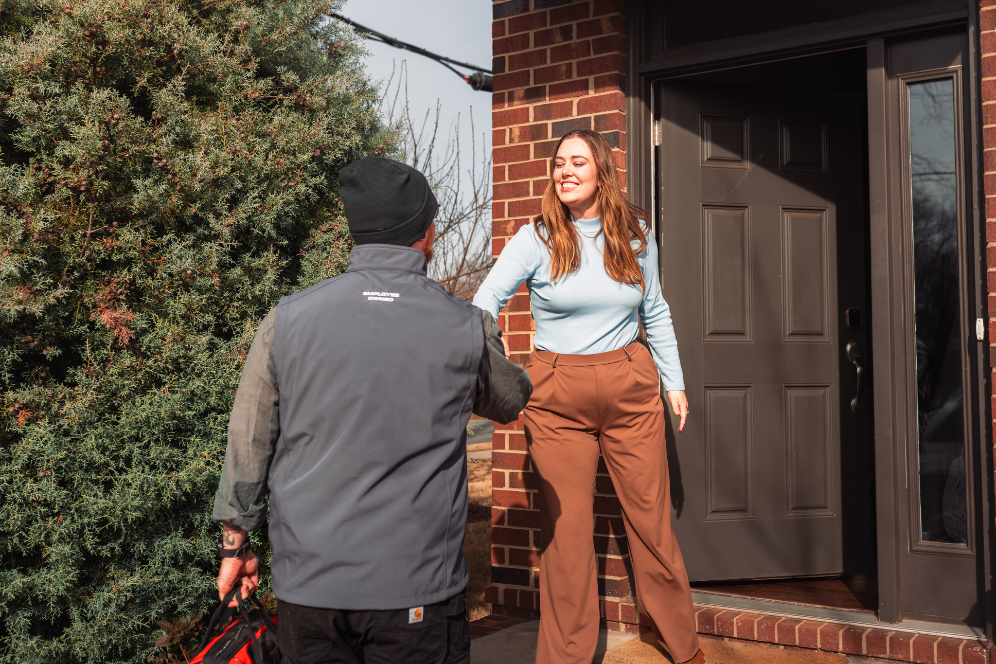 Charlotte Mechanical technician Raynor meeting a customer at the front door of their home, reaching forward to shake hands with the customer.