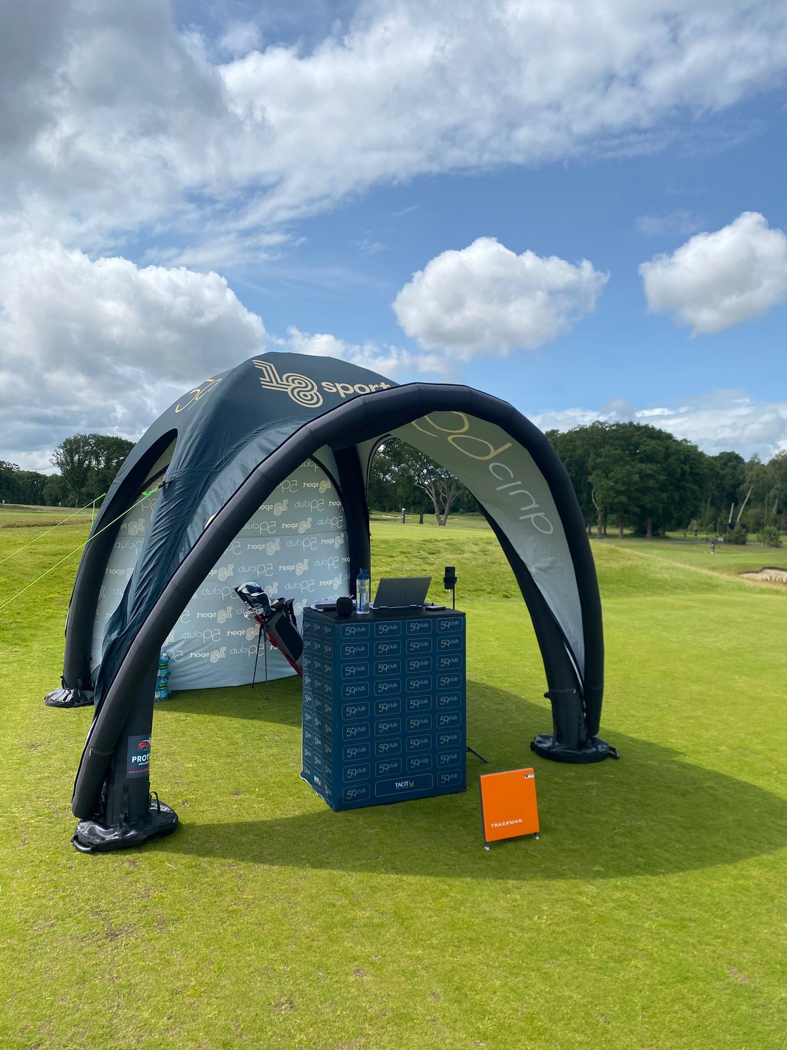 Inflatable tent with 18-Sport branding on a golf course green under a partly cloudy sky.