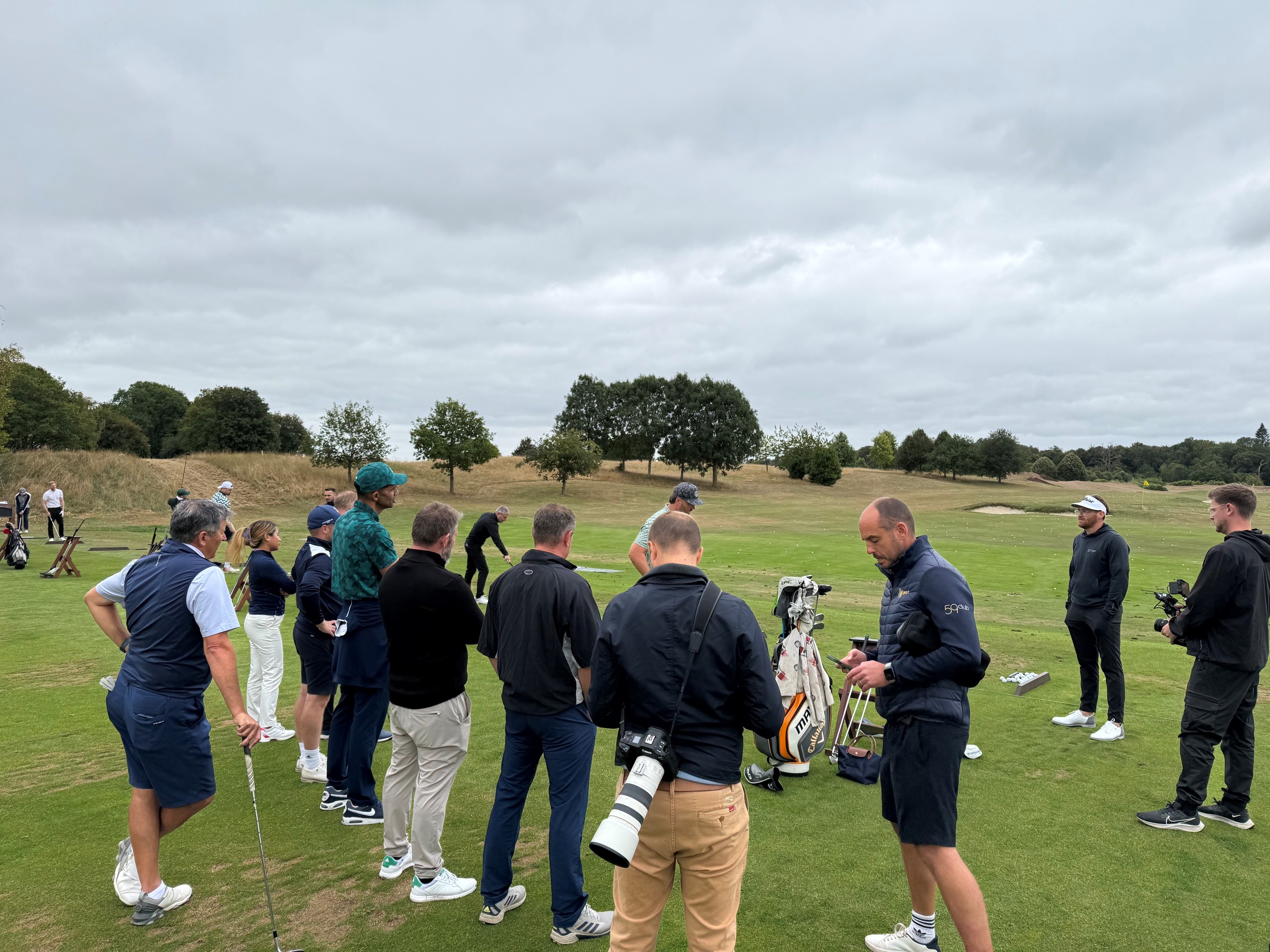 Group of people on a golf course watching a golfer prepare to hit a shot on a cloudy day.